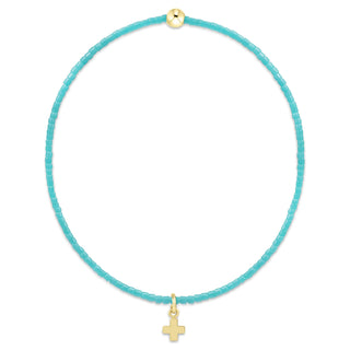 Turquoise cord necklace with a gold cross pendant on a white background