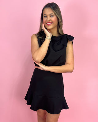 Woman wearing a black dress with ruffled details against a pink background