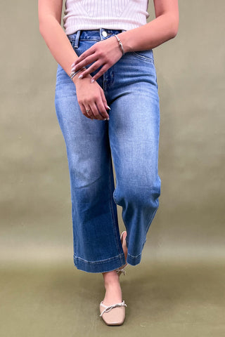 Person wearing blue jeans and a white top on a beige background