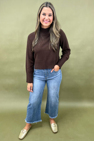 Chocolate brown mock neck sweater styled with light wash wide leg frayed hem jeans and gold loafers