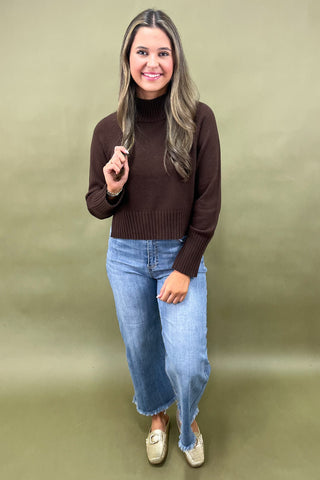 Chocolate brown mock neck sweater styled with light wash wide leg frayed hem jeans and gold loafers