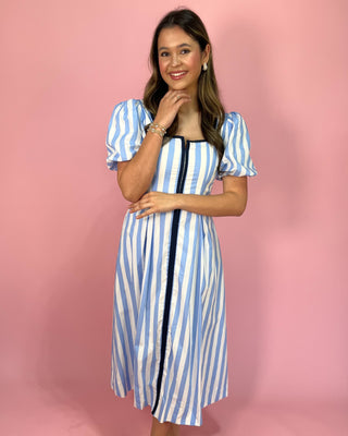 Woman wearing a blue and white striped dress against a pink background