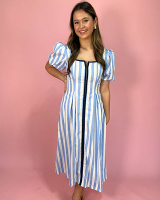 Woman wearing a blue and white striped dress with puff sleeves against a pink background