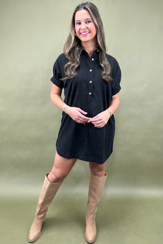 Woman wearing a black dress and beige boots against a green background