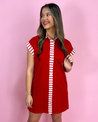 Woman wearing a red dress with white striped details against a pink background