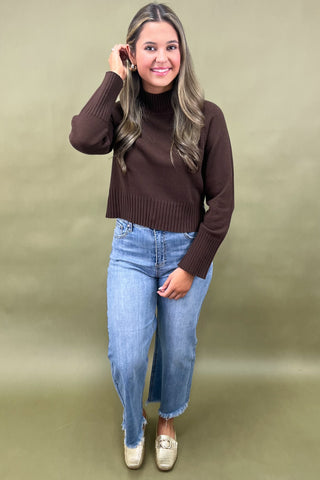 Chocolate brown mock neck sweater styled with light wash wide leg frayed hem jeans and gold loafers