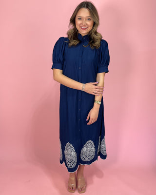 Woman wearing a blue dress with white embroidery on a pink background
