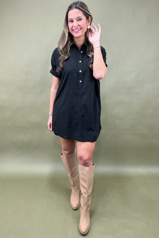 Woman wearing a black dress and beige knee-high boots against a plain background