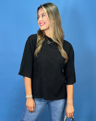 A woman wearing a black short-sleeve top and blue jeans, standing against a solid blue background.