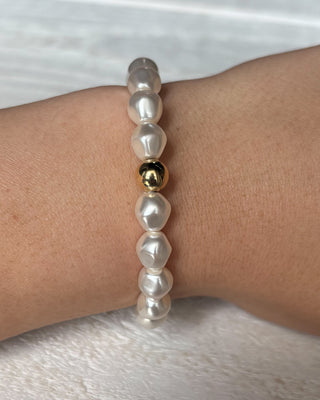 Pearl bracelet with a gold bead on a wrist against a white background