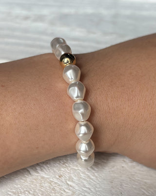 Pearl bracelet on a wrist with a gold clasp against a light background