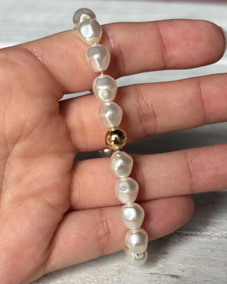 Pearl bracelet with a gold bead held in a hand on a light wooden surface