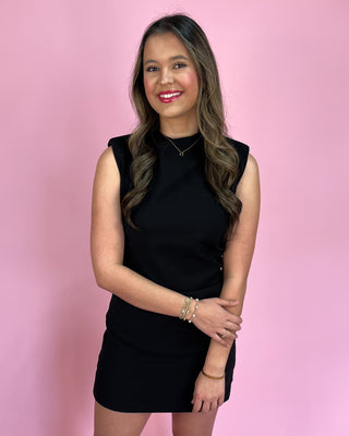 Woman wearing a black sleeveless dress against a pink background