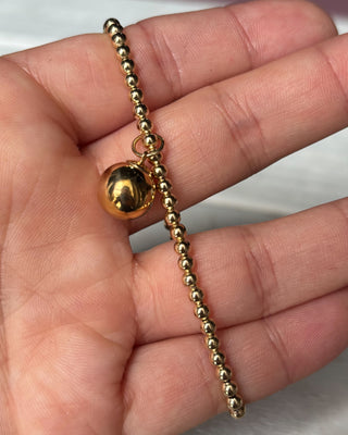 Gold beaded bracelet on a hand against a white background