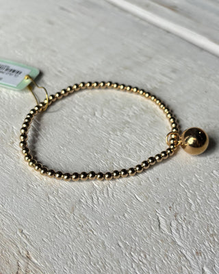Gold beaded bracelet with a tag on a light gray surface
