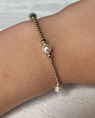 Gold bracelet with pearls on a wrist against a neutral background