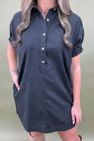 Person wearing a dark denim shirt dress against a plain background