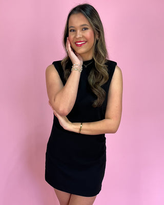 Woman in a black dress posing against a pink background