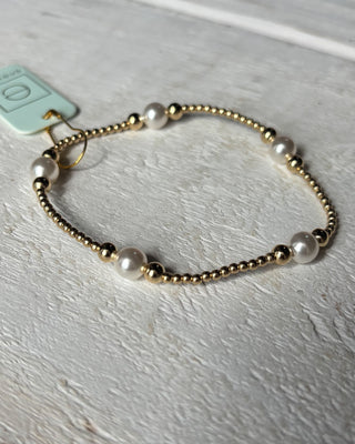 Bracelet with gold beads and pearls on a light gray background