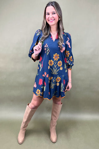Woman wearing a blue floral dress with beige boots against a plain background