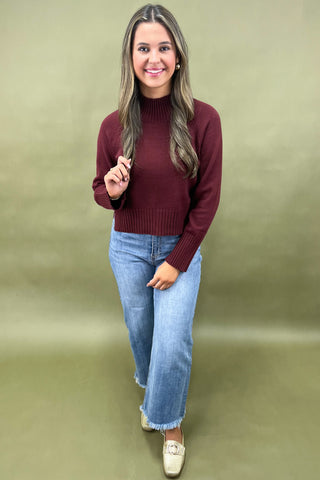 Burgundy mock neck sweater styled with light wash wide leg frayed hem jeans and gold loafers