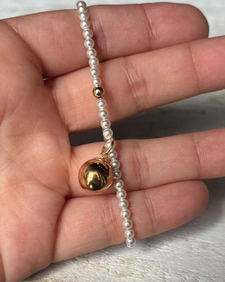 Pearl bracelet with a gold bead held in a hand on a light background
