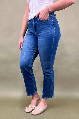 Person wearing blue jeans and a white top on a plain background