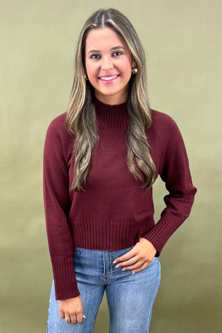 Burgundy mock neck sweater styled with light wash wide leg frayed hem jeans and gold loafers