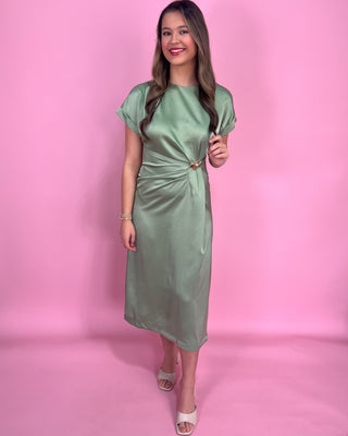 Woman wearing a green satin dress with gold accents against a plain background
