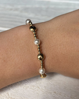 Bracelet with gold and pearl beads on a wrist against a light background
