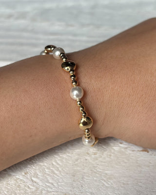 Gold and pearl bracelet on a wrist against a light background