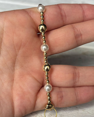 Gold and pearl beaded bracelet on a hand against a neutral background