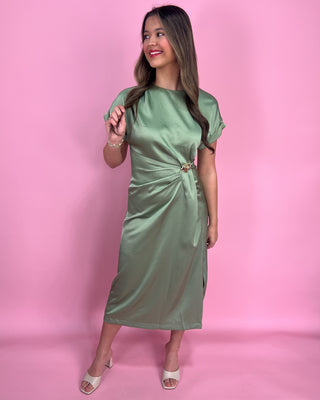 Woman wearing a green satin dress with gold accents against a plain background