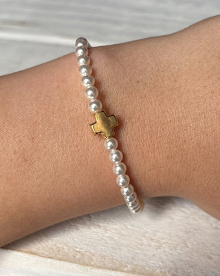Pearl bracelet with a gold cross on a wrist against a neutral background