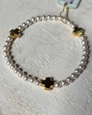 Pearl bracelet with gold and black cross charms on a light wooden surface
