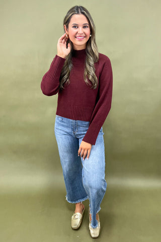 Burgundy mock neck sweater styled with light wash wide leg frayed hem jeans and gold loafers