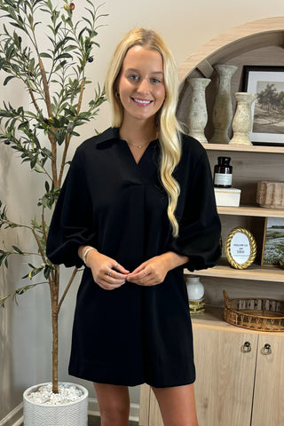 Woman in a black dress standing in a room with decor elements.