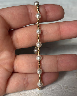 Pearl and gold beaded bracelet on a hand against a neutral background
