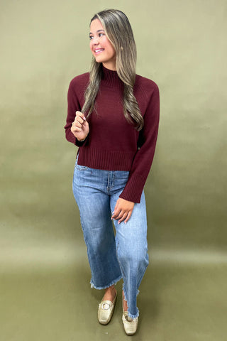 Burgundy mock neck sweater styled with light wash wide leg frayed hem jeans and gold loafers