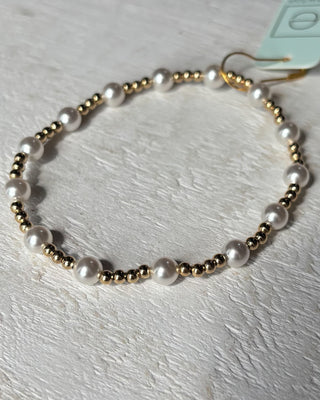 Bracelet with alternating gold and pearl beads on a light wooden surface