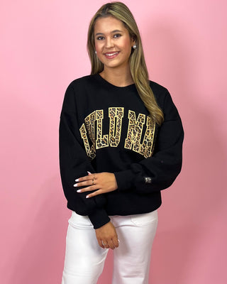 Woman wearing a black sweatshirt with gold lettering against a pink background