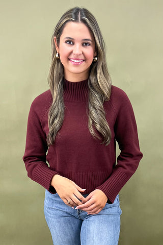 Burgundy mock neck sweater styled with light wash wide leg frayed hem jeans and gold loafers