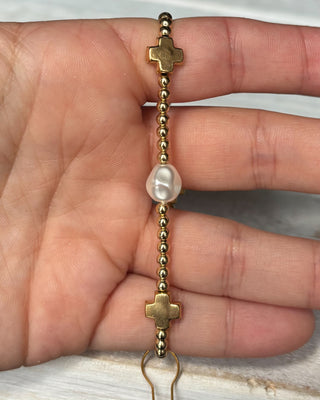 Gold bracelet with pearls held between fingers against a neutral background