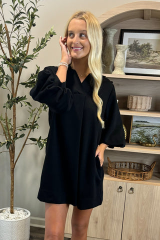 Woman in a black dress standing in a room with decor elements.