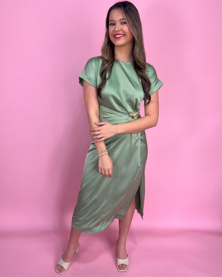 Woman wearing a green satin dress with gold accents against a plain background