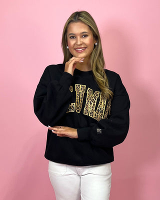 Woman wearing a black sweatshirt with gold lettering against a pink background