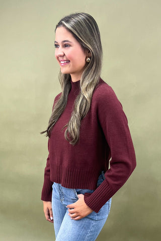 Burgundy mock neck sweater styled with light wash wide leg frayed hem jeans and gold loafers