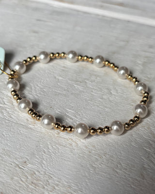 Bracelet with alternating gold and pearl beads on a light wooden surface