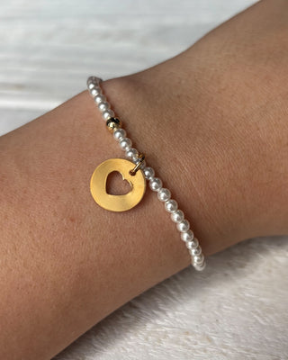 Pearl bracelet with a gold heart pendant on a pink background