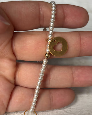 Pearl bracelet with a gold heart pendant on a pink background